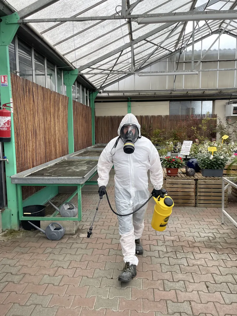 Technicien 3DTECH marchant avec un pulvérisateur jaune devant les tables de culture d’une jardinerie