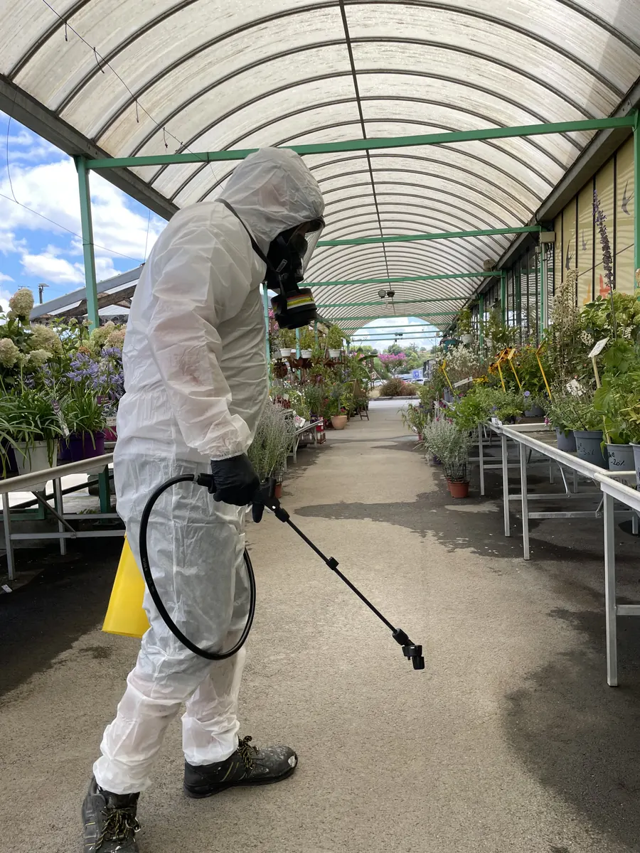 Technicien 3DTECH dans l’allée d’une serre de jardinerie, entre les plantes en pot