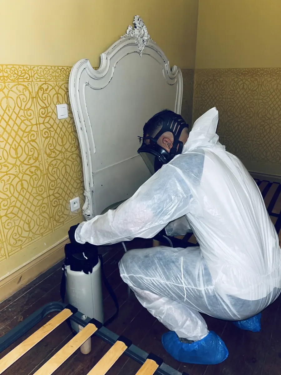 Technicien accroupi qui traite le pied et l’arrière d’une tête de lit contre les punaises de lit